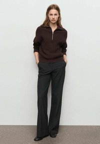 Sude color marrón oscuro con canalé y cremallera a la cuarta, combinado con pantalones de pierna ancha en color gris carbón y zapatos planos negros, todo sobre un fondo neutro.