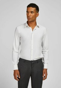 Chemise blanche à boutons avec manches longues, texture lisse et col classique, assortie à un pantalon gris foncé. Design minimaliste, coupe ajustée.