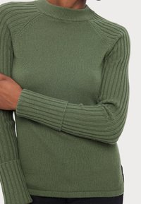 Pull vert en tricot côtelé avec un col montant, des manches ajustées et des accents texturés sur les épaules. Matière douce et coupe classique.