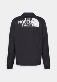 Veste noire à manches longues avec poignets élastiques, affichant un grand logo blanc "THE NORTH FACE" et emblème sur le haut du dos.