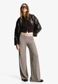 Brown leather jacket over a black ribbed crop top and striped wide-leg pants. Dark sunglasses complete the look.