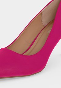 Φούξια γόβα με λεπτή μύτη, μπεζ επένδυση εσωτερικά και λεία επιφάνεια, σε λευκό φόντο.