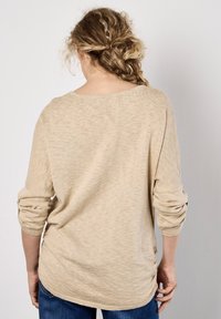 Beige, långärmad topp i en strukturerad stickad design, med vid halsringning och avslappnad passform, med uppvikta ärmar och en böjd nederkant.