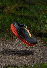 Baskets de course légères avec une tige noire, des accents orange et un design texturé. Elles présentent une semelle rouge proéminente et des lacets contrastants.