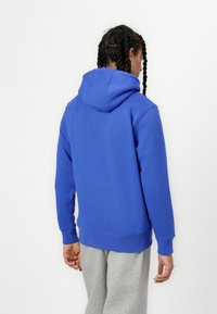 Sweatshirt azul com capuz feito de tecido macio, apresentando um bolso canguru e punhos canelados, combinado com calças de moletom cinza claro.