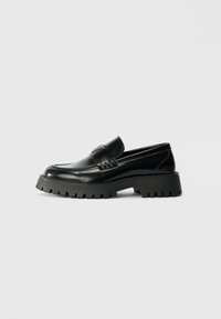 Black leather loafers with a chunky, textured rubber sole, featuring a front strap and subtle logo detail on the heel.