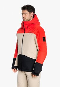 Rot, beige und schwarz gefärbte Winterjacke mit Kapuze, Reißverschluss und Logo-Patch an den Ärmeln, aus isolierendem Material gefertigt.