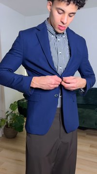Navy blue blazer with a tailored fit, worn over a black and white checkered shirt, buttoning at the front. Brown pants visible. Indoor setting.