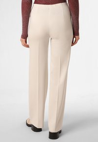 Beige hochgeschnittene Hose mit glatter Textur, geradem Bein-Design und zwei Gesäßtaschen, kombiniert mit hellfarbigem Schuhwerk.