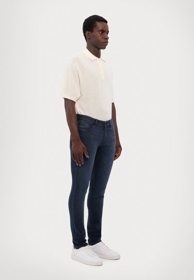 White knit polo shirt with short sleeves and a collar, paired with dark blue slim-fit jeans and white sneakers.