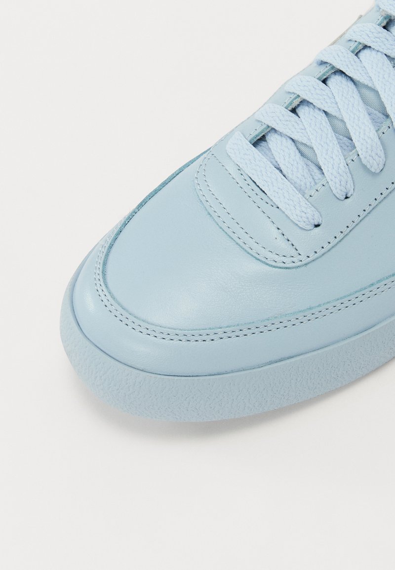 Baskets en cuir bleu clair avec une texture lisse, bout rond, semelle plate et fines lacets bleu clair. Des coutures subtiles sont visibles.
