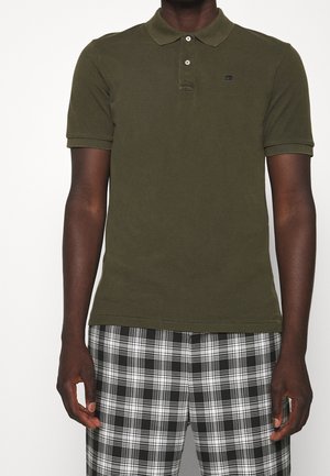 Polo verde oliva con cuello, tapeta de dos botones y logotipo bordado, combinado con pantalones cortos a cuadros en negro y blanco.