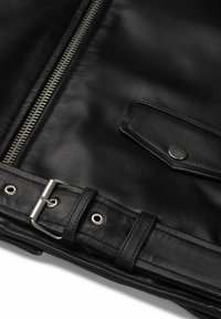 Giacca di pelle nera con zip argentata, tasca con bottone a scatto e dettagli con cintura, caratterizzata da hardware in metallo e occhielli. Texture liscia.