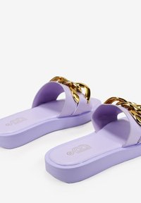Chanclas moradas con un detalle de cadena dorada brillante en la parte superior. Fabricadas en plástico suave, con suela plana y forma redondeada.