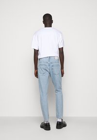 Jeans de color azul claro con un corte recto, que presentan bolsillos traseros, detalles de lavado sutiles, y una camiseta blanca, combinados con zapatos negros.