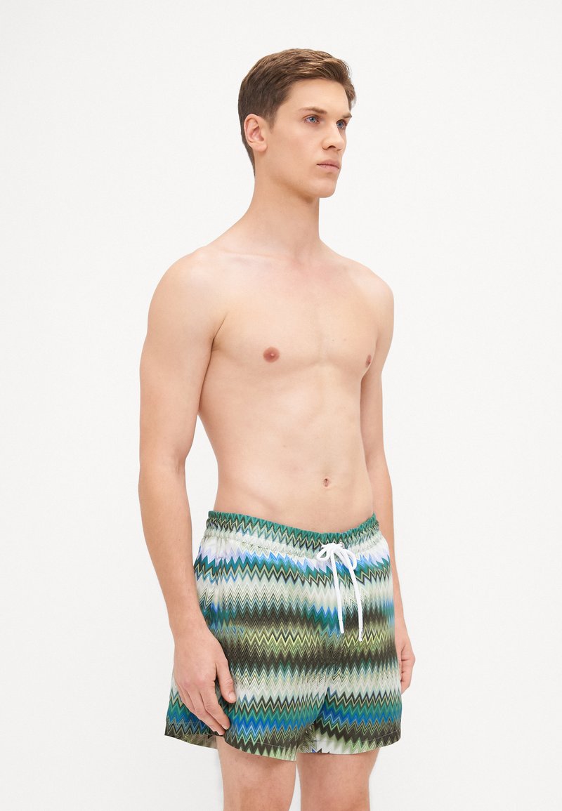 Svømmedragter med zigzag-mønster i blå, grøn og brun. Lavet af letvægtsmateriale, med elastisk talje og snor.