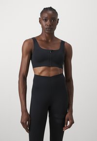 Melna sporta krūšturis ar priekšējo rāvējslēdzēja slēgšanu, platām siksnām un pieguļošu dizainu. Gluda tekstūra ar niecīgām perforācijām visā audumā.