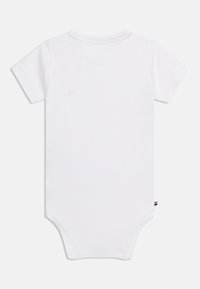 Λευκό βρεφικό φορμάκι με κοντά μανίκια και στρογγυλή λαιμόκοψη, που δείχνει την πίσω όψη και μια μικρή πλαϊνή ετικέτα με κόκκινες, λευκές και μπλε ρίγες.