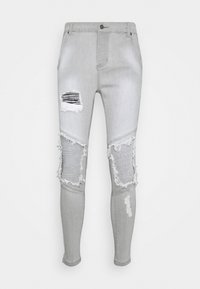 Světlé šedé skinny džíny s několika trhlinami a třepícími se okraji. Obsahují horizontální žebrovaný vzor na koleni. Vyrobeno z denimového materiálu.