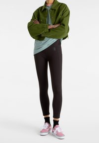 Leggings neri a vestibilità aderente con cuciture grigie, abbinati a una giacca di jeans verde e una t-shirt azzurro chiaro, completati da sneakers rosa.