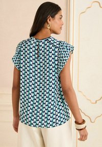 Kortärmad blus med hjärtmönster i ljusblått och marinblått. Har volangärmar och en nyckelhålsöppning i ryggen. Slät tygkvalitet.