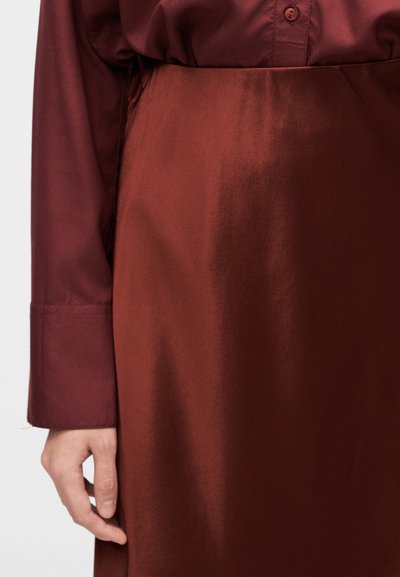 Spódnica z bordo satyny o gładkiej fakturze, z wysokim stanem i detalem na szwie bocznym, zestawiona z pasującą błyszczącą koszulą z długim rękawem.