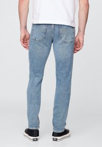 Világoskék farmernadrág karcsúsított szabással, hátul zsebekkel és enyhe kifakulással. Fekete sportcipővel és fehér pólóval viselve.