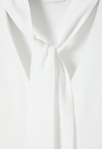 Blouse blanche avec un détail de cravate en tissu doux nouée en un nœud lâche au col avant.