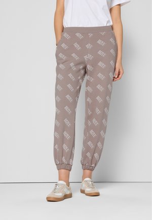 Szare dresy z białym nadrukiem "BIZUU" w całej powierzchni, z elastycznym paskiem w talii i elastycznymi mankietami, zestawione z jasnymi sneakersami.