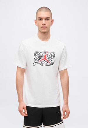 Mann trägt weißes T-Shirt mit roter Basketball-Silhouette und schwarzem Ornament-Design, kombiniert mit schwarzen Shorts mit weißem Besatz.