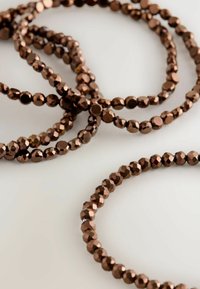 Bronzefarbene Perlenstränge mit facettierten runden und hexagonalen Formen, die in der Größe variieren und eine glänzende Oberflächenstruktur aufweisen.