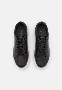 Černé kožené tenisky s hladkým svrškem, šněrováním, lehkým polstrováním a bílými gumovými podrážkami. Logo "Calvin Klein" na stélkách.