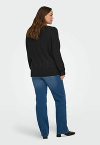 Black cable-knit sweater with long sleeves, paired with blue jeans and black ankle boots. Visible ribbed hem and texture details.