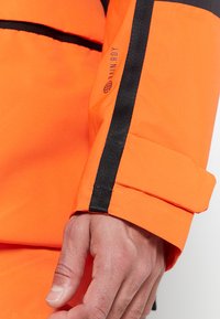 Bright orange waterproof jacket with black accents. Features a sleek design, adjustable cuff, and subtle branding on the sleeve.