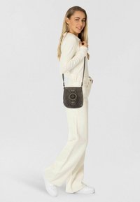 Borsa a tracolla grigia con motivo circolare decorativo; texture morbida, tracolla regolabile e forma compatta. Indossata a spalla.