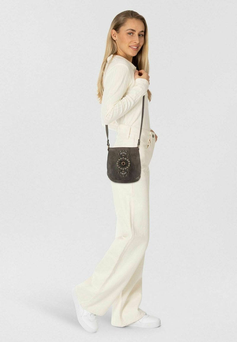 Borsa a tracolla grigia con motivo circolare decorativo; texture morbida, tracolla regolabile e forma compatta. Indossata a spalla.