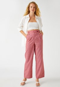 Pantalones rosas de pierna ancha con una tela texturada, que cuentan con una cintura alta, pliegues y bolsillos laterales, combinados con un top corto blanco y una camisa abotonada.
