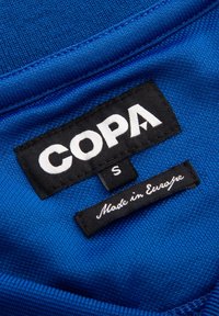 Kleidungslabel auf blauem Stoff mit Marke "COPA,", Größe klein "S," und "Made in Europe" Text in Weiß auf schwarzen Etiketten.