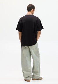 T-shirt nera oversize in cotone, abbinata a jeans baggy verde chiaro e calzature marroni. Modello visto da dietro.
