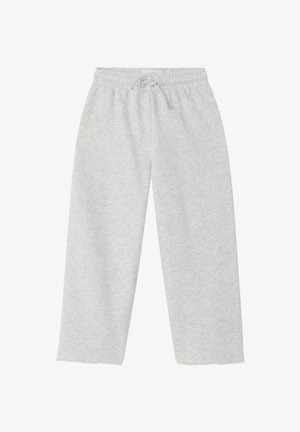 Bambino con pantaloni della tuta grigio chiaro e sneakers bianche e nere, in piedi contro uno sfondo chiaro e uniforme.