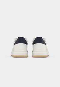 Pair of white low-top sneakers with black heel tabs and gum rubber soles, shown from the back against a plain white background.