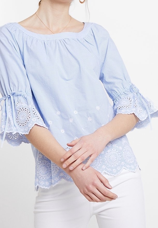 Light blue striped blouse with embroidered lace trim and bell sleeves. Features a rounded neckline and floral accents on the fabric.