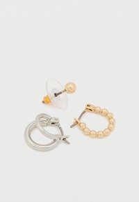 Tri náušnice: jedna priehľadná s guľôčkou zo zlata, jedna strieborná kruhová, a jedna zlatá kruhová s korálkou a zapínaním. Rôzne tvary a kovové povrchy.