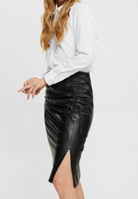 Gonna a tubino in finta pelle nera con dettagli arricciati e uno spacco laterale, abbinata a una camicia bianca con bottoni. Tessuto morbido e design aderente.
