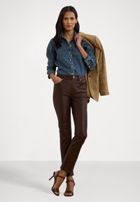 Hnedé kožené nohavice, modrá denimová košeľa a štruktúrovaný béžový blejzer. Čierne sandále na vysokých podpätkoch dotvárajú outfit. Minimalistický dizajn, priliehavý strih.