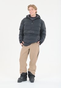 Schwarze, plüschige Jacke mit Reißverschlusskragen und "SLOPE"-Logo, kombiniert mit beigen, wasserdichten Hosen mit schwarzen Akzenten und Reißverschlüssen.
