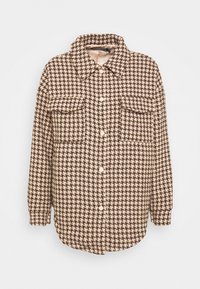 Hnědá a béžová košile s límečkem a vzorem houndstooth, s předním zapínáním na knoflíky a dvěma náprsními kapsami. Měkká textilní struktura.