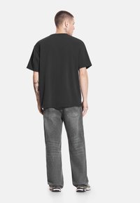 Czarny bawełniany t-shirt z okrągłym dekoltem i krótkimi rękawami, zestawiony z szarymi dżinsami o luźnym kroju i spranym efekcie.