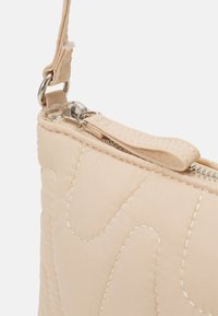 Borsa trapuntata beige con superficie texturizzata, dotata di una zip argentata, un tirante per la zip e un anello metallico per il trasporto.