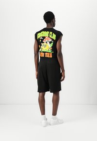Black sleeveless graphic t-shirt featuring colorful designs and text on the back, paired with black mesh shorts and white sneakers.